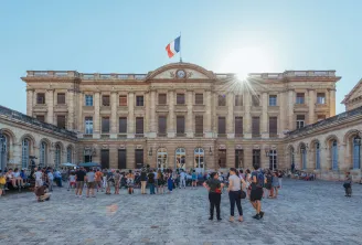 Facciata del Palazzo Rohan a Bordeaux con il suo cortile pavimentato, architettura classica in pietra, bandiera francese in cima e visitatori nel cortile in una giornata di sole.