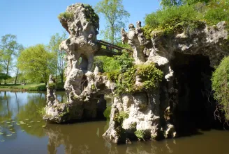 Rovine di pietra bianca con un arco ricoperto di muschio accanto a uno stagno, circondate da lussureggiante vegetazione verde nel Parco Majolan di Bordeaux.