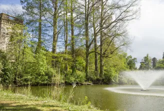 Vista del Parco di Bourran a Bordeaux con una torre di pietra storica, un lago con fontana, alberi maestosi e vegetazione lussureggiante primaverile.