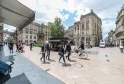 Piazza animata di Bordeaux con pedoni, ciclisti e negozi, circondata da edifici in stile hausmanniano sotto un cielo nuvoloso.