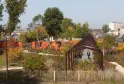 Vista del Parco aux Angéliques a Bordeaux con pergolato in legno, vegetazione autunnale colorata, recinzione bianca in primo piano e la Garonna sullo sfondo