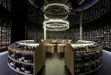 Cantina di vini moderna del Latitude 20 Wine Bar a Bordeaux, con scaffali curvi pieni di bottiglie di vino, un bancone centrale in legno e illuminazione circolare bianca al soffitto.