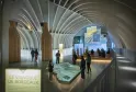 Interno della Cité du Vin a Bordeaux con architettura moderna a soffitto bianco lucido ad arco, visitatori che osservano un modello illuminato del vigneto di Bordeaux e schermi espositivi sulle pareti.