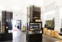 Interno moderno della Max Bordeaux Wine Gallery & Cellar con vetrine illuminate di bottiglie di vino, casse di legno impilate e attrezzature di degustazione in uno spazio luminoso e minimalista.