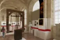 Interno del Museo Nazionale delle Dogane di Bordeaux che presenta un'esposizione con una bilancia storica in legno, pannelli informativi con bande rosse, ritratti e oggetti doganali in una galleria voltata.