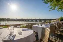 Terrazza del ristorante sulla Garonna a Bordeaux con tavoli apparecchiati, vista sul ponte di Pietra e lo skyline della città con cielo soleggiato