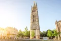 La Torre Pey-Berland, un campanile gotico del XV secolo a Bordeaux, con guglie ornamentali e una statua dorata in cima, circondata da edifici storici e alberi.